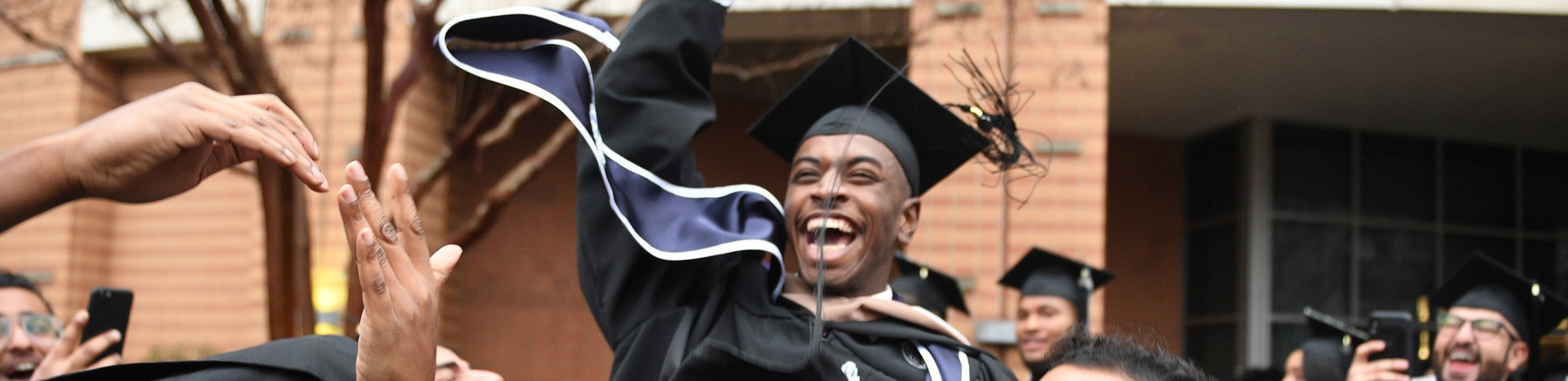 Graduate laughs as he is lifted up by his fellow graduates