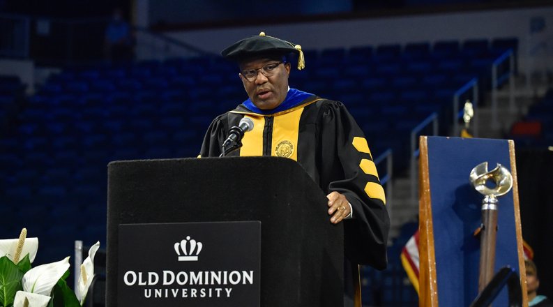 A man delivers a commencement speech from a lectern while wearing a robe.