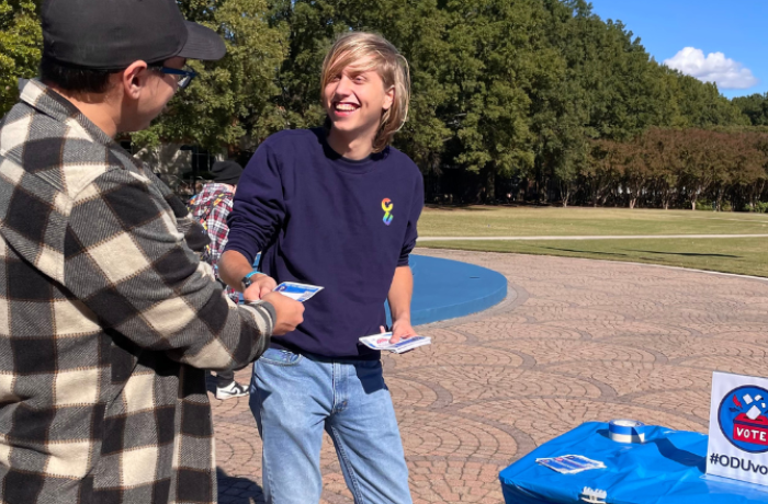 A student hands out a flyer to another student on ODU's campus.