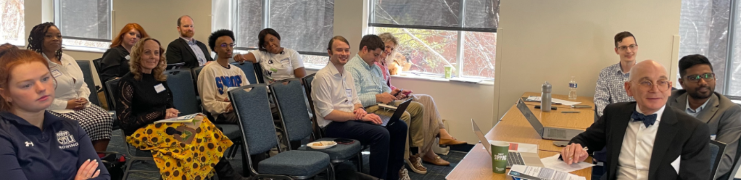 Men and women sit in chairs in conference room.
