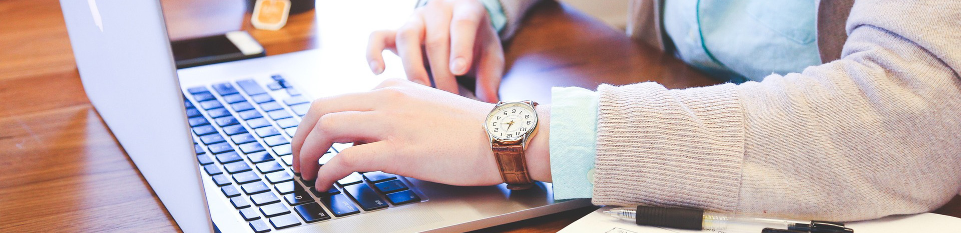Hands typing on a laptop. Person wearing analog watch.