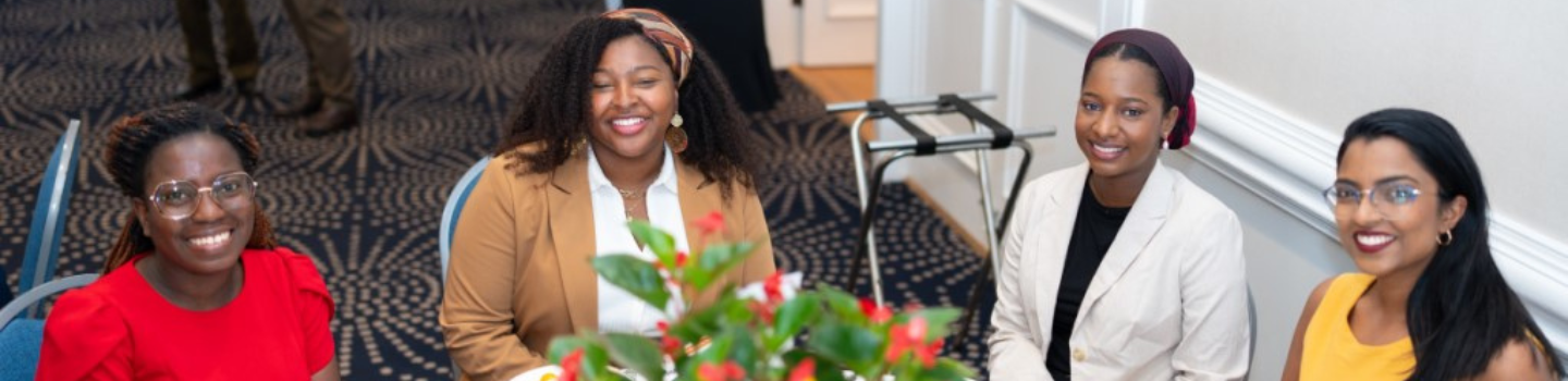 Four students sitting at table during luncheon smile for photo.