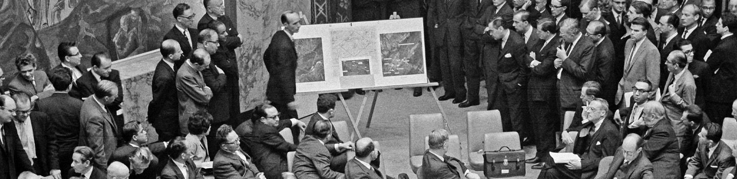 Black and white photo shows UN reviewing aerial photos of Cuban missiles in 1962.