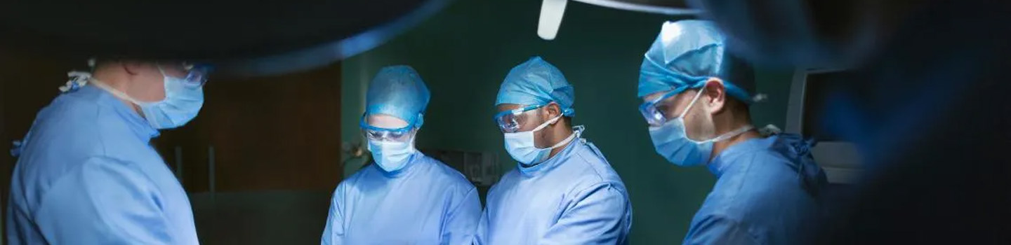 Team of four doctors work on patient in dark operating room.
