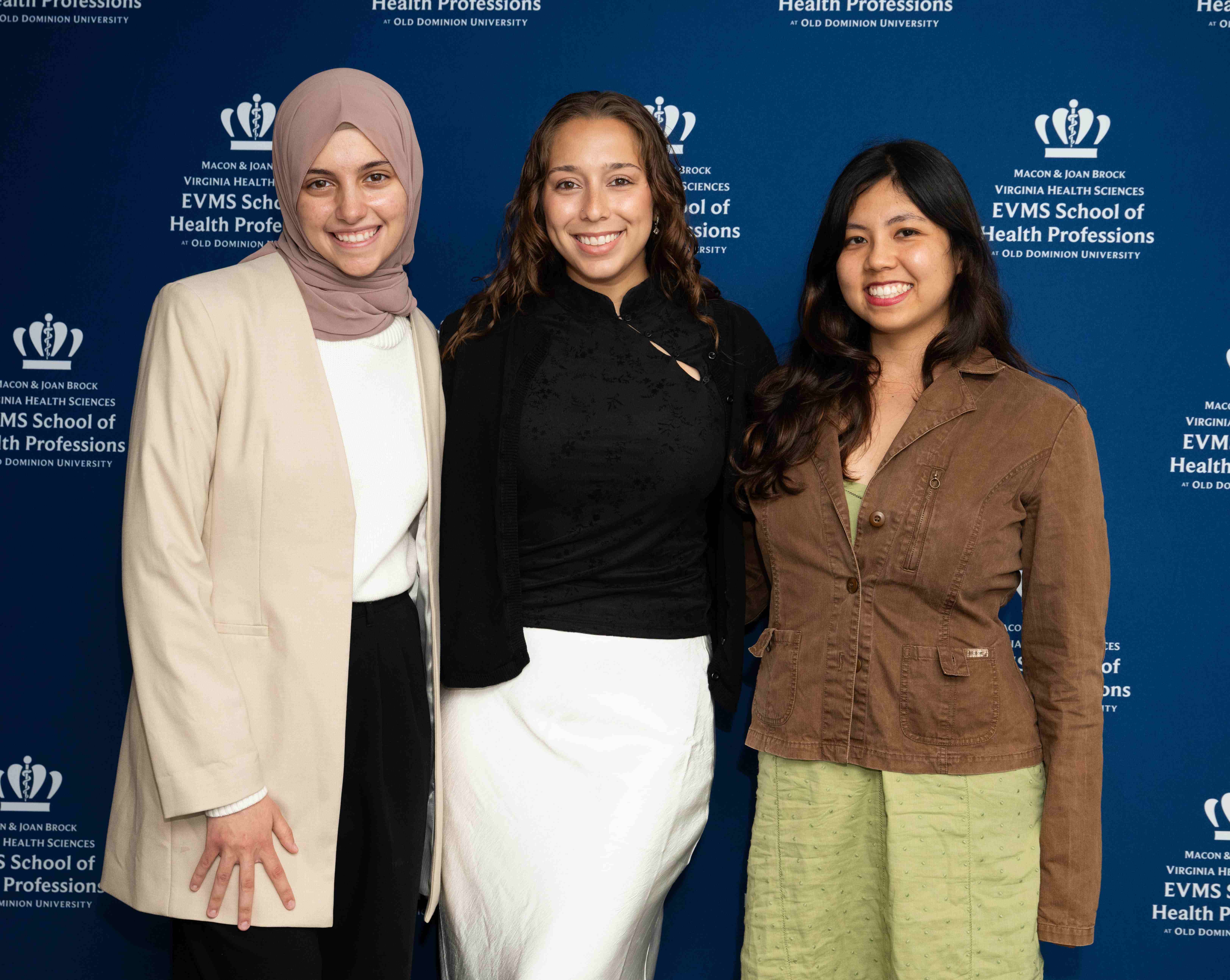 2026 M1 Student Research Participants from right to left: Jillian Gallardo, Thalia Hoyos, and Israa Saleh standing in front of an EVMS Health Professions backdrop. 