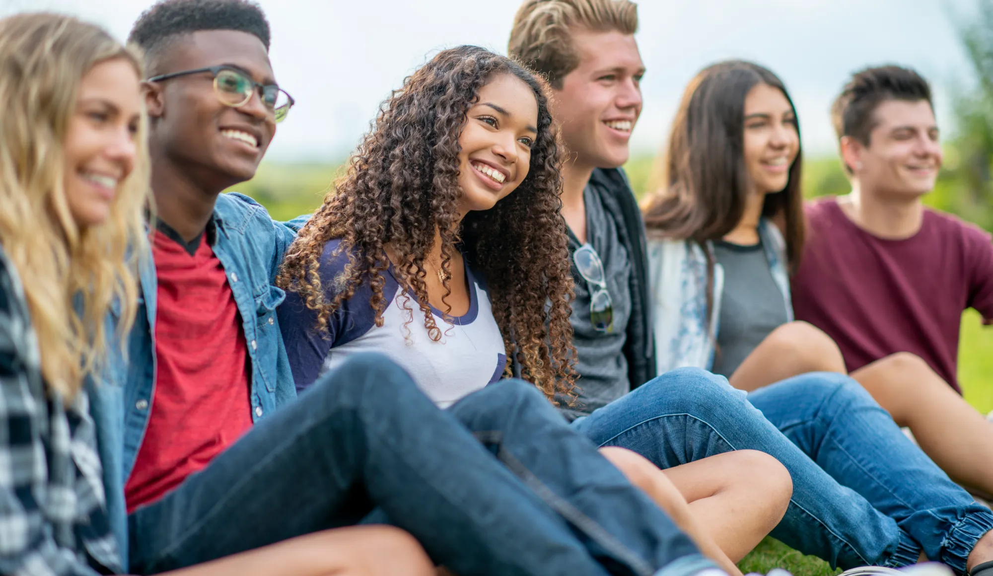 A small group of teenagers sit in the grass as they hang out