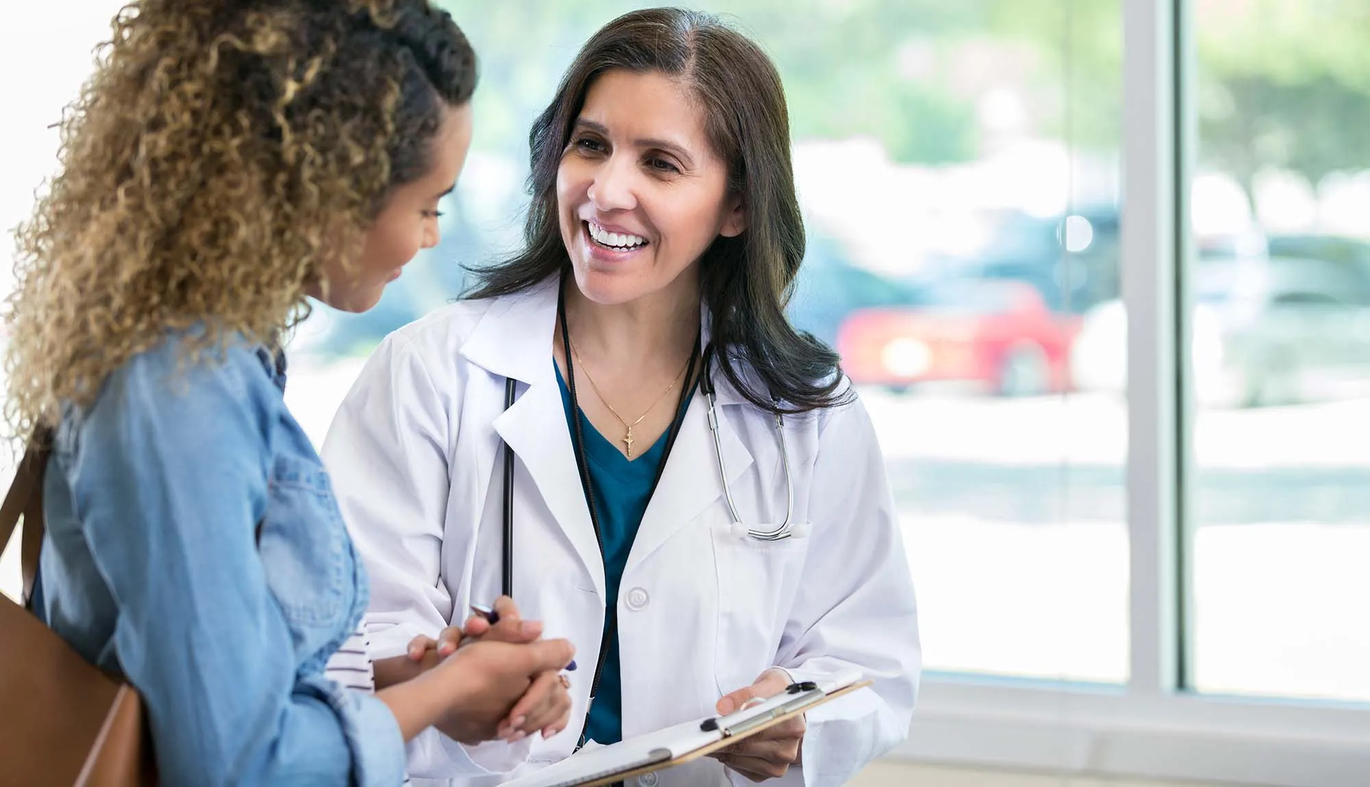 A female doctor holding a clipboard speaks to a patient.