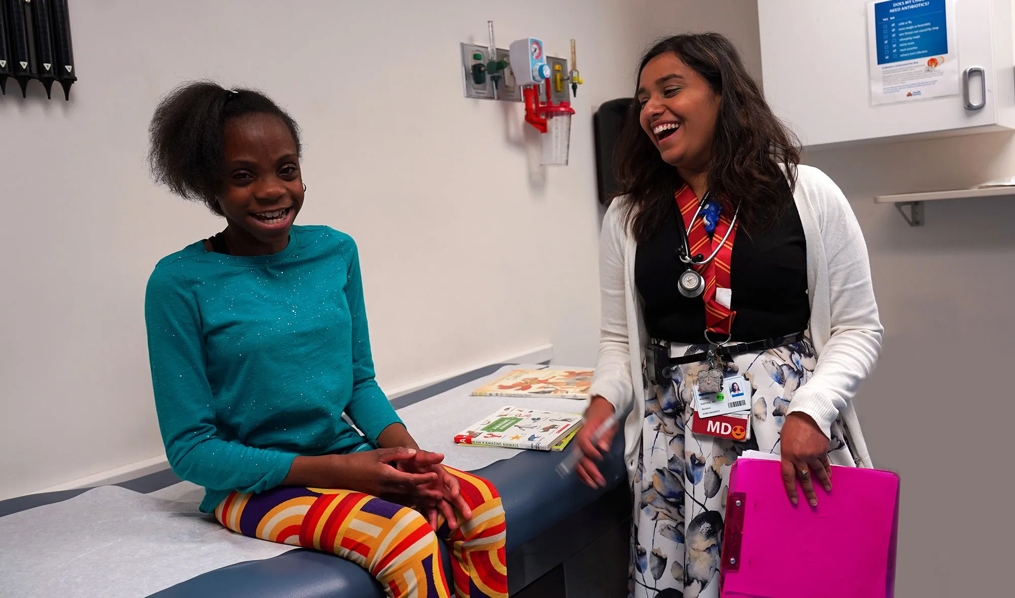 Dr. Kapoor laughs with a young girl, who is smiling while wa