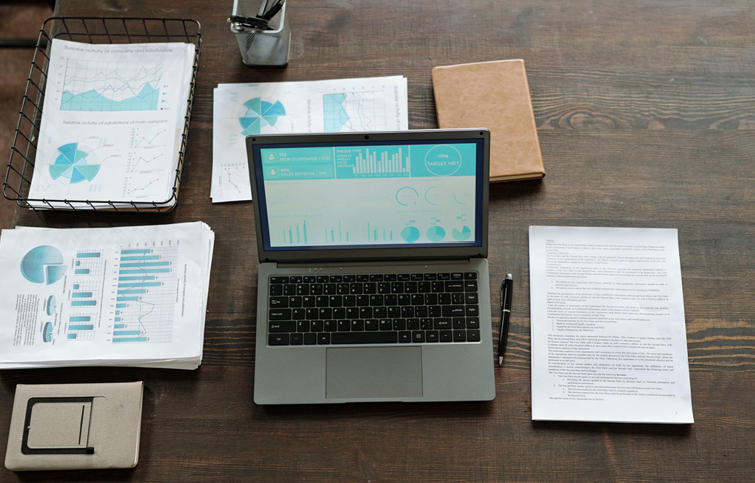 Pile of papers, notes, and a laptop on a desk. 
