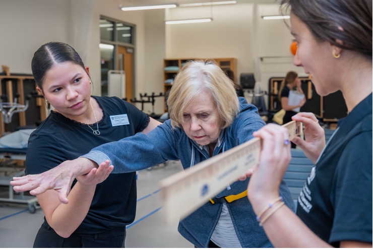Two medical professionals help elderly woman with her balance.