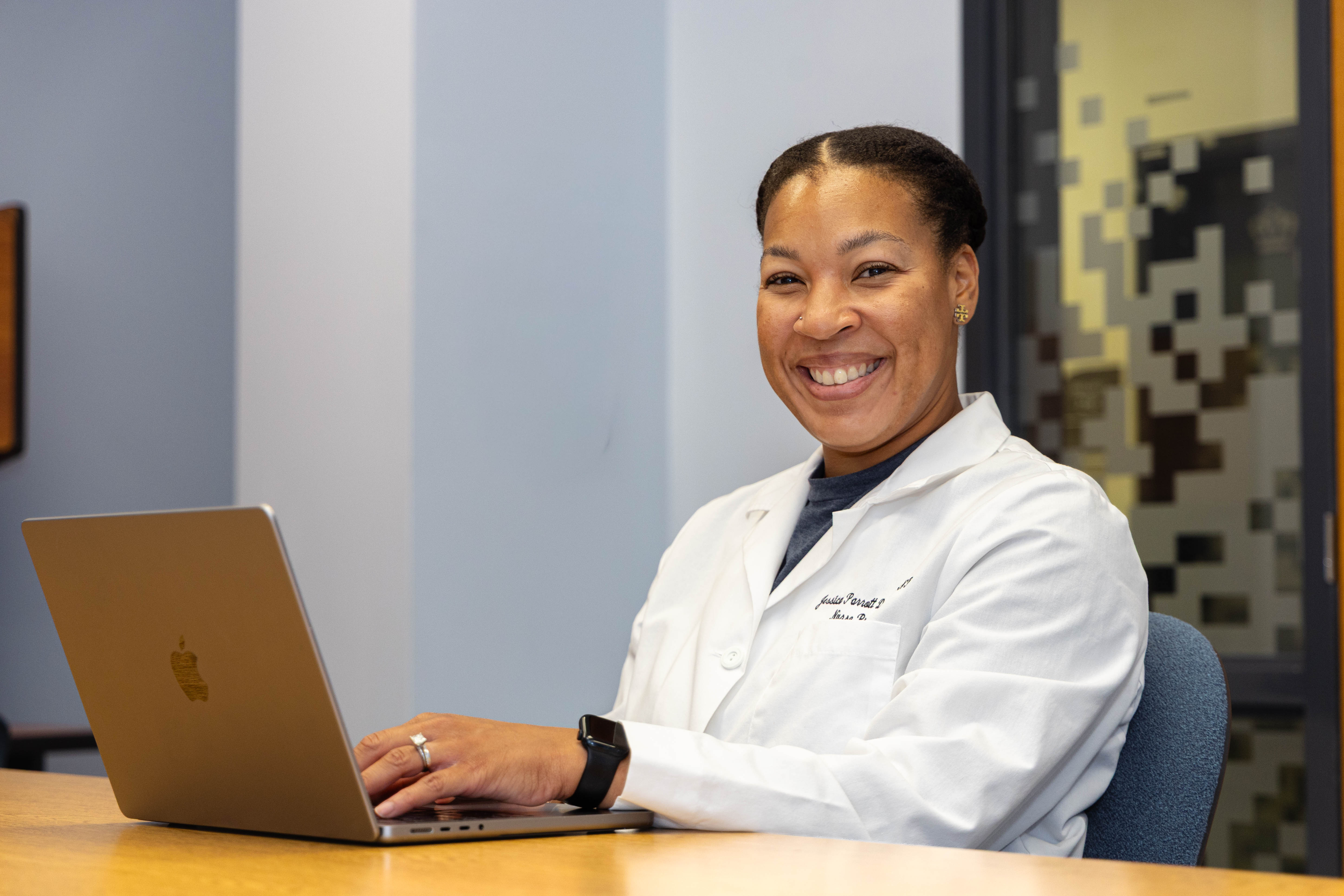Nursing student smiles while sitting at a desk with laptop.