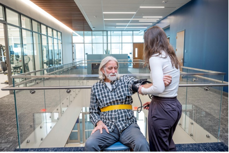 Man sits in chair while woman measures his blood pressure.