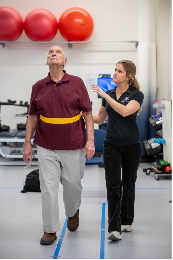 Physical therapy clinician helps elderly patient with his balance.