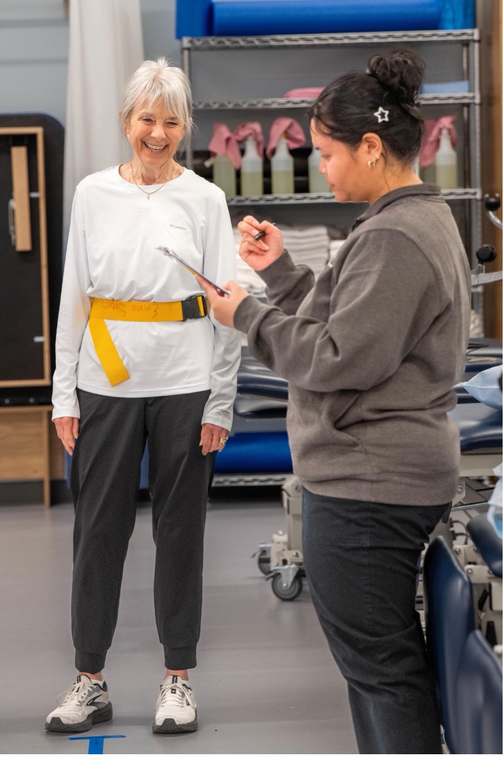 Female clinician writes on clipboard during physical therapy session with elderly woman.