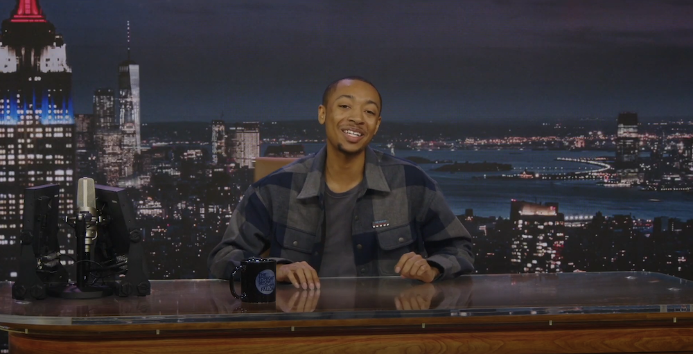Student seated behind talk show host’s desk in television studio.