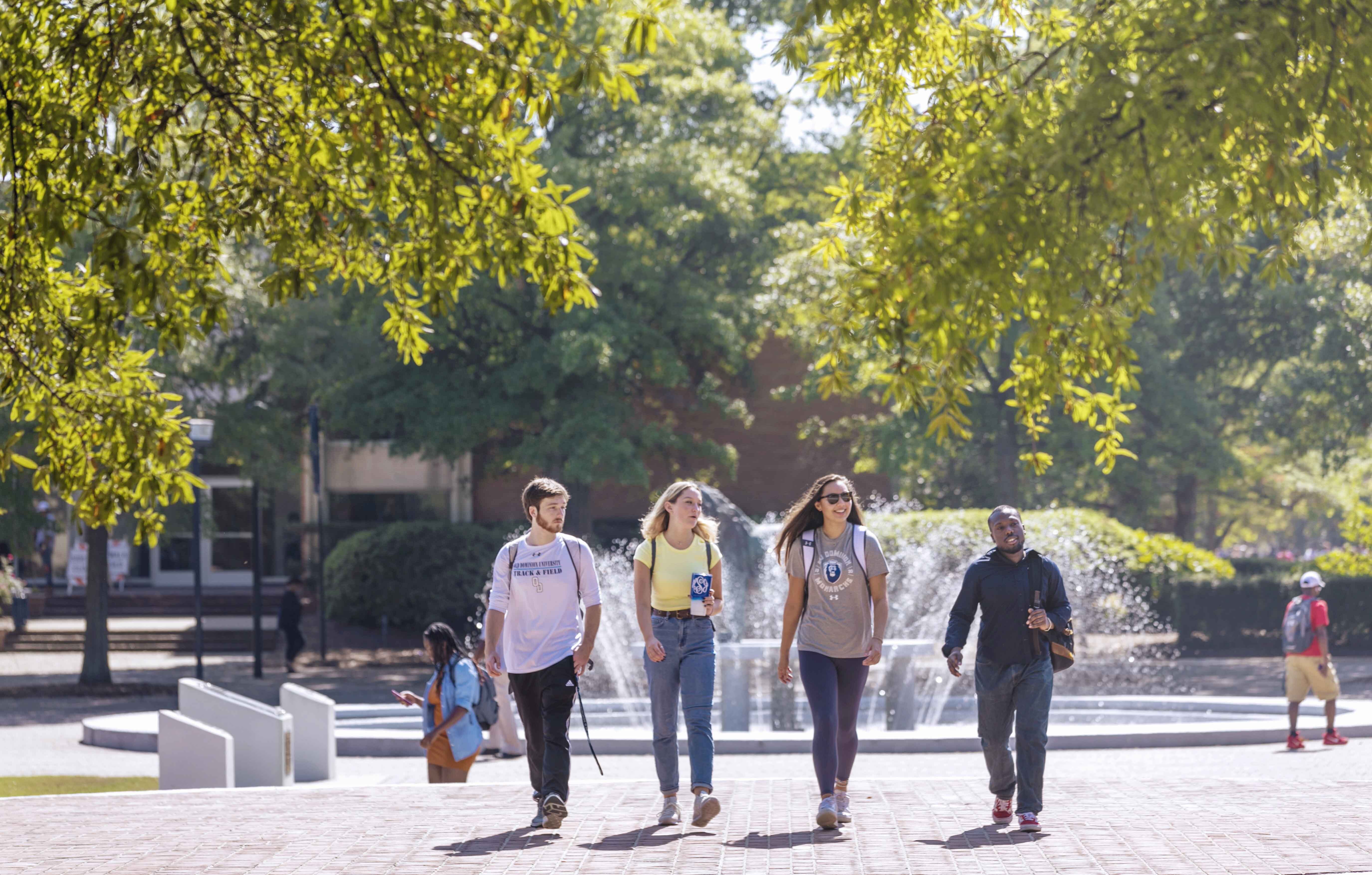 A group of students walk on ODU's campus in front of the lion fountain. 