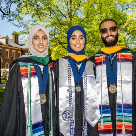 Sana, Seena and Fozi Alkaifi pose in graduation regalia with Rollins Hall in the background.