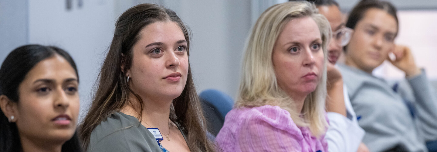 Row of students sit at table during presentation.