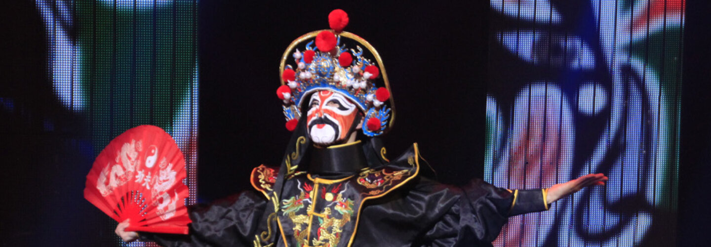 Three performers wear traditional asian attire on stage during theater performance