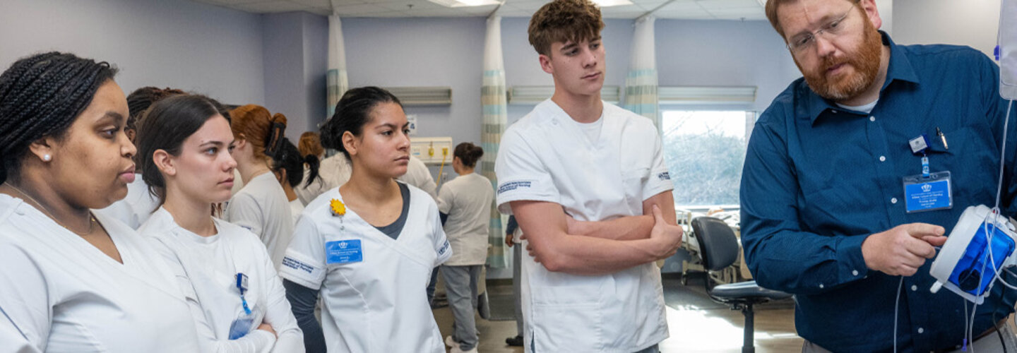 Nursing students in medical simulation lab watch instructor use medical device.