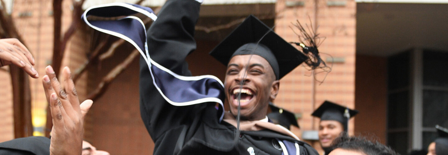 Graduate laughs as he is lifted up by his fellow graduates
