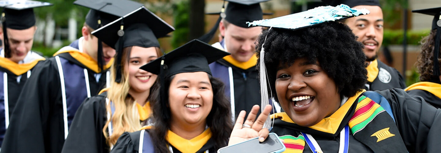 Black female graduate waves at photographer in procession