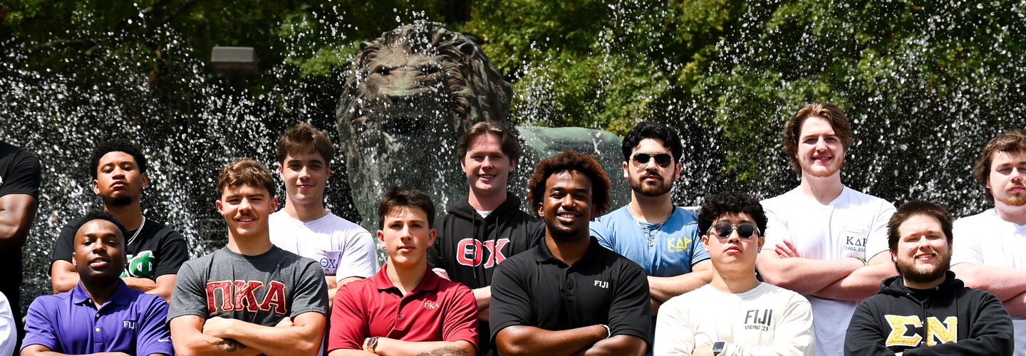 Students in Fraternity Shirts stand in front of a fountain