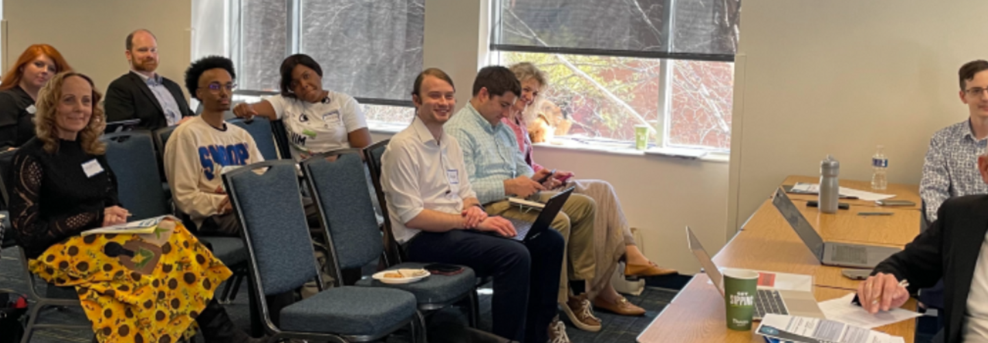 Men and women sit in chairs in conference room.