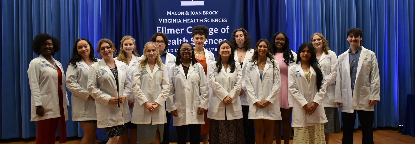 MLS Students stand in white coats in front of a banner