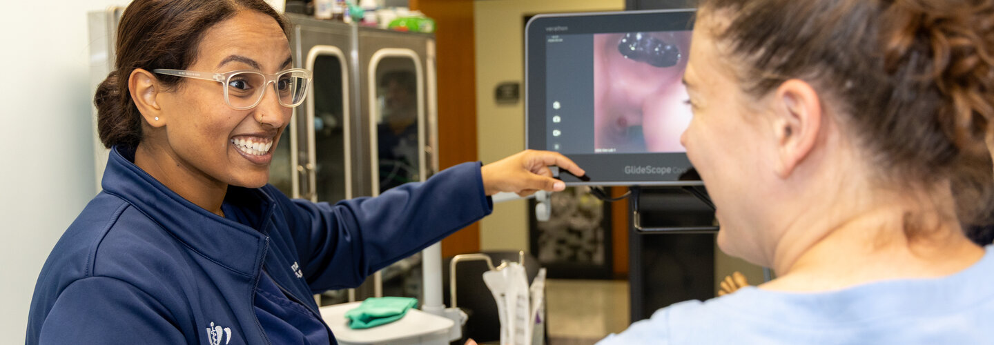 Two nursing students smile at each other while reviewing images on medical device screen.