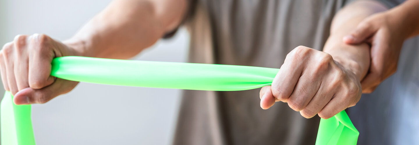 Physical Therapist helps male patient use resistance band