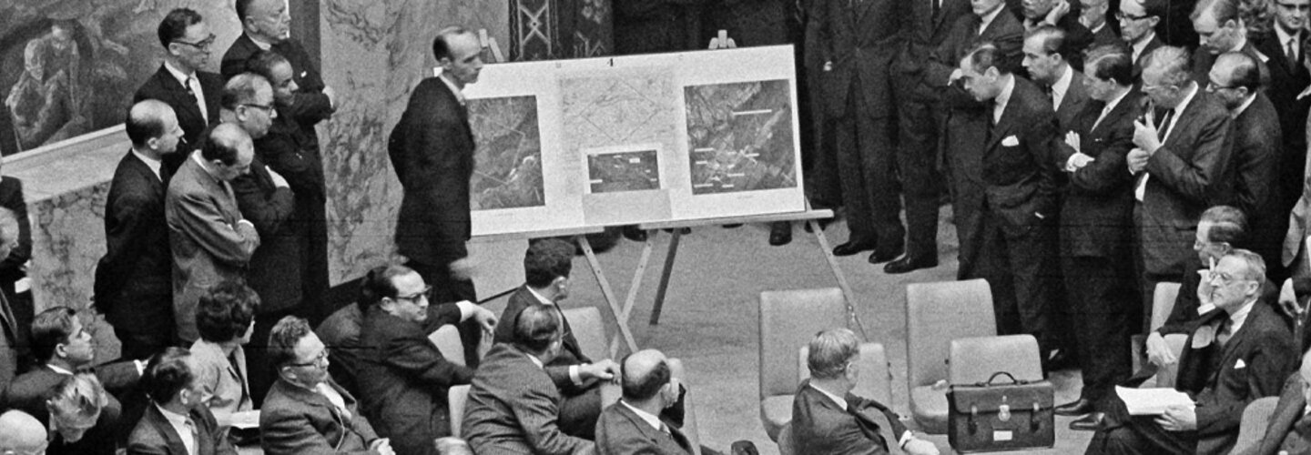 Black and white photo shows UN reviewing aerial photos of Cuban missiles in 1962.