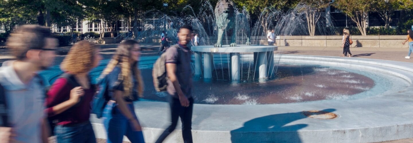 Students blurred walking across campus in front of Lion fountain. 