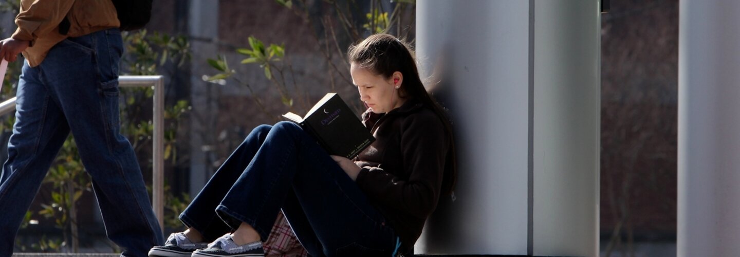 Student on steps reading a book on a windy and cold day.