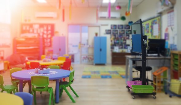 Early childhood classroom with small tables and chairs, play mats and teaching monitor.