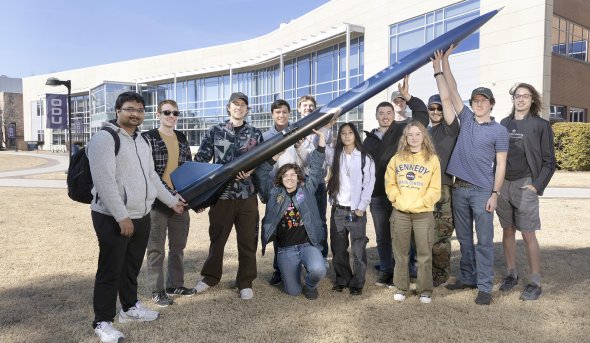 Group of students holding a 10-foot rocket outside