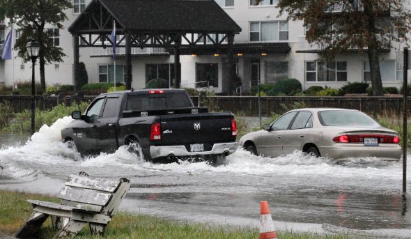 a black pick-up truck and a white sedan drive through a flooded street