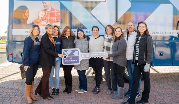 A group of women stand together in front of ODU's mobile health van. 