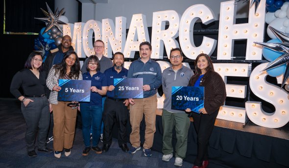 People standing in front of a sign reading "Monarch Milestones" while holding signs.