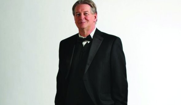 ODU alumnus Eric Feber stands in a white room wearing a tuxedo. 