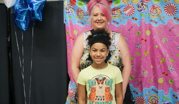 An adult and a child stand smiling in front of a colorful candy-themed backdrop.