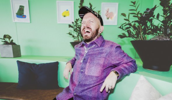 ODU alumnus Nigel Tierney sits on a couch, laughing 