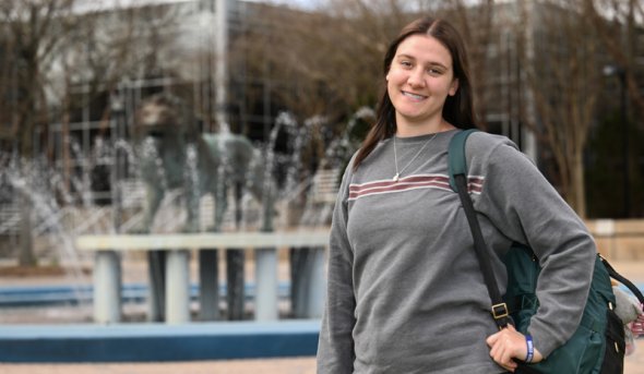 Amie Burdette stands in front of the Old Dominion University lion fountain, holding a backpack and smiling.
