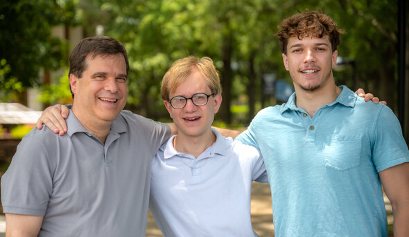 Three smiling men stand with their arms around each other on the Old Dominion University campus. 