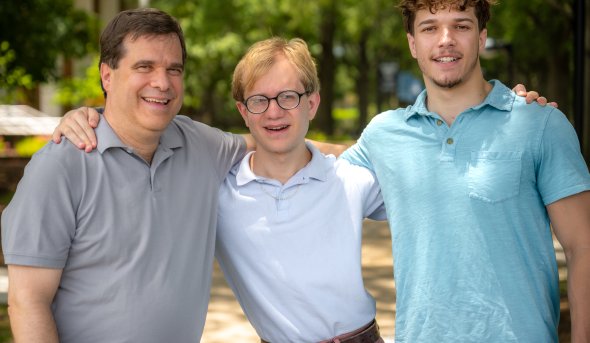 Three smiling men stand with their arms around each other on the Old Dominion University campus. 