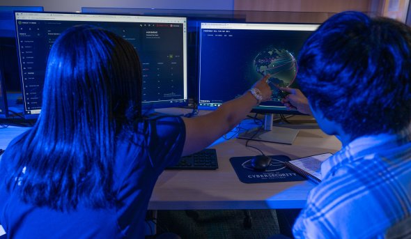 Two people in a dark room looking at computer monitors