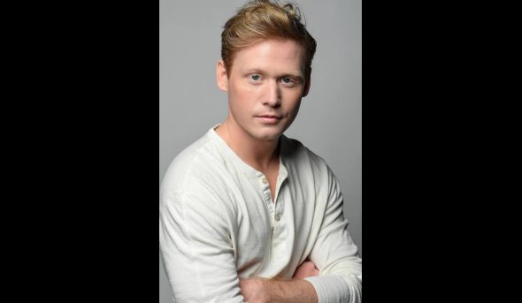 A man wearing a white shirt, standing and looking directly at the camera.
