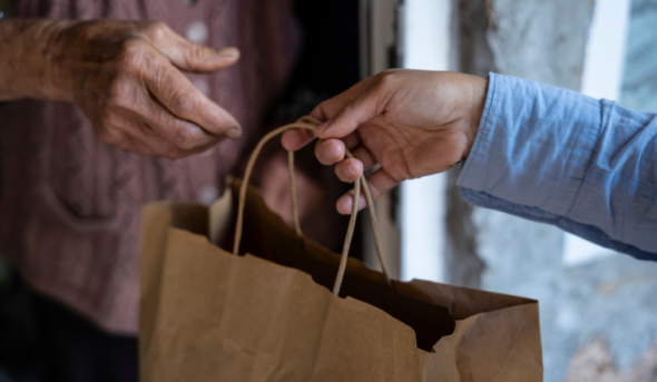 Two hands exchange a paper grocery bag.