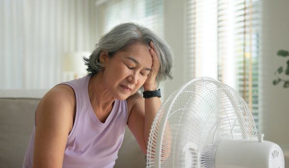 Woman sits on couch with electric fan blowing on her face.