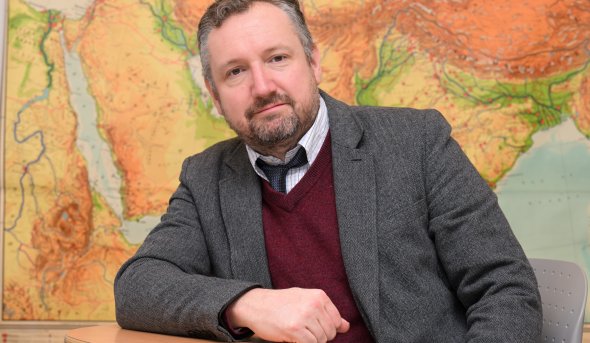 Jared Benton, Ph.D., an ODU associate professor, sits at a table in front of a world map. 